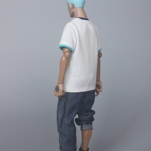 May include: A white t-shirt with a teal trim around the collar and sleeves. The t-shirt is being worn by a person with blue hair and blue jeans. The person is wearing white and brown sneakers.
