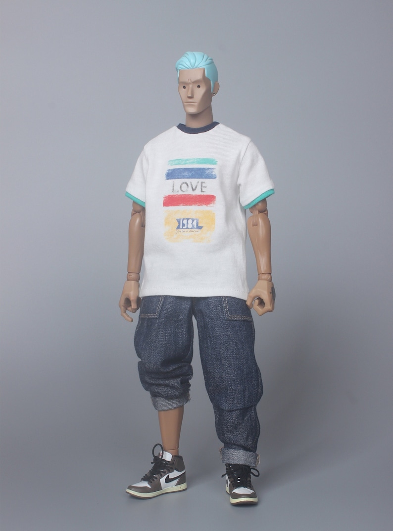 May include: A white t-shirt with a colorful graphic print that says "LOVE 1984". The model is wearing blue jeans and white sneakers.
