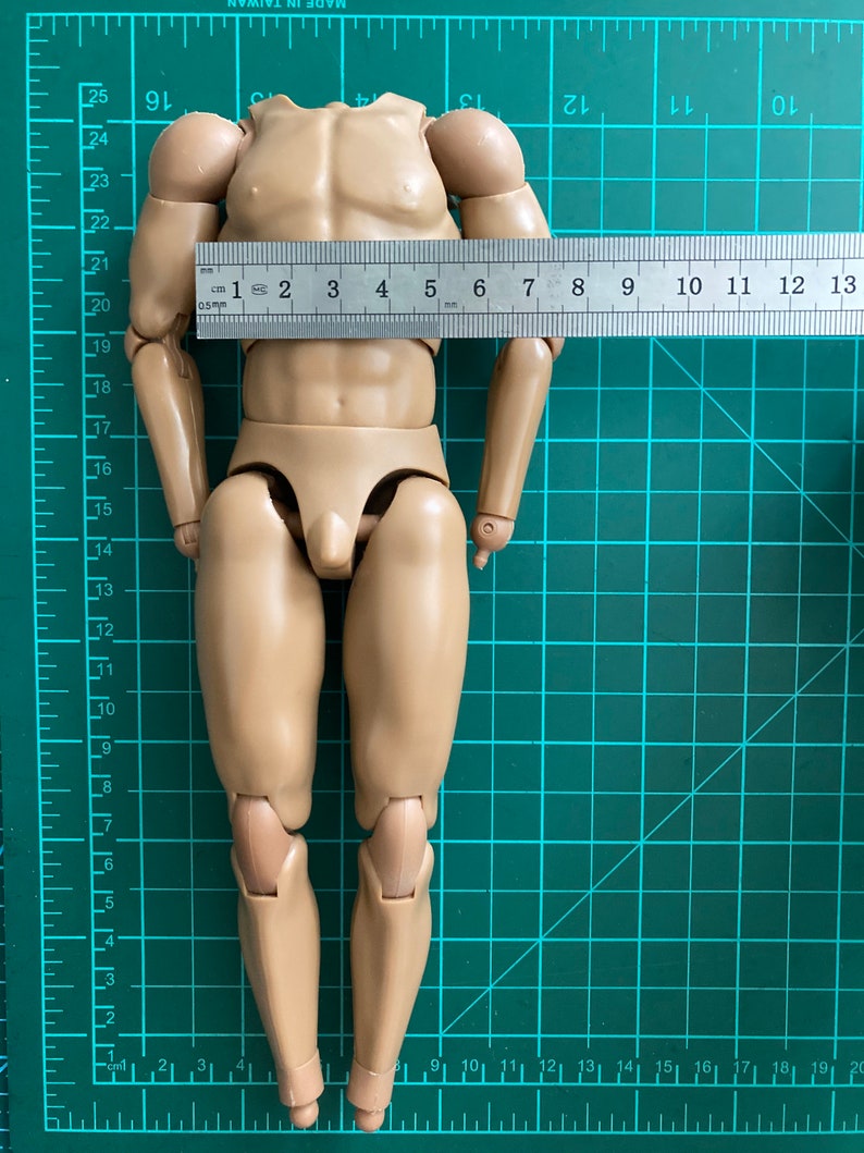 May include: A nude-colored plastic action figure with articulated limbs. The figure is standing on a green gridded mat with a ruler measuring 13 cm in length.