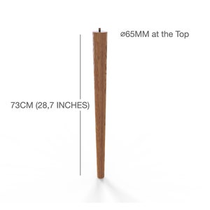 May include: A tapered wooden furniture leg with a natural wood grain finish. The leg measures 28.7 inches in height and has a diameter of 65mm at the top. A small metal mounting bolt is visible at the center of the top surface of the leg.