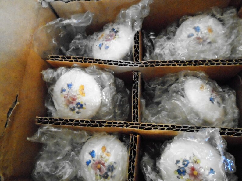 Pu&ograve; includere: Una scatola di cartone contenente diversi pomelli per armadietti in ceramica bianca. Ogni pomello &egrave; decorato con un motivo floreale nei toni del blu, giallo e rosa. I pomelli sono avvolti singolarmente in plastica trasparente.