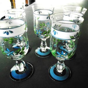 May include: Set of six clear glass wine glasses with hand-painted blue and green floral designs. Each glass has a white band with a blue trim around the middle.
