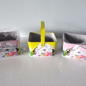 May include: Three Easter baskets, one yellow and two pink, with bunny and egg designs. The baskets are made of metal and have handles.