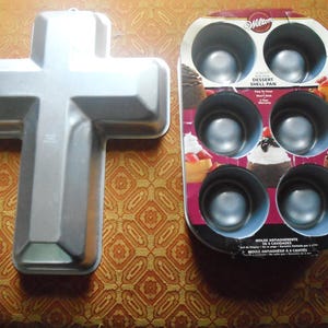 May include: A silver-colored, cross-shaped baking pan and a six-cavity dessert shell pan. The cross pan is made of metal. The shell pan is in a cardboard package with images of desserts.