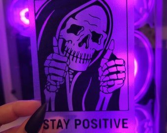 May include: A black and white sticker featuring a cartoon image of the Grim Reaper giving a thumbs up. The text "STAY POSITIVE" is printed below the image.