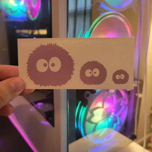 May include: Three white vinyl stickers featuring a fluffy, purple, cartoon character with large eyes. The stickers are different sizes, with the largest sticker in the center and the two smaller stickers on either side.