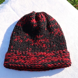 May include: A hand-knitted beanie hat in black and red. The hat features a ribbed brim in alternating black and red stitches, with a body of the hat in a speckled pattern of black and red yarn. The hat is made of a soft, warm material.
