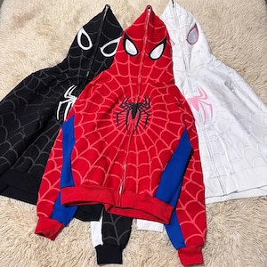 May include: Three full-zip hoodies featuring a hood that zips up to cover the face with mesh eye openings. The hoodies come in black, red with blue side panels, and white, each decorated with a spiderweb pattern and a large spider chest emblem.