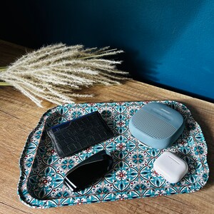 May include: A blue and white patterned tray with a black leather wallet, a blue speaker, and a white wireless earbud.