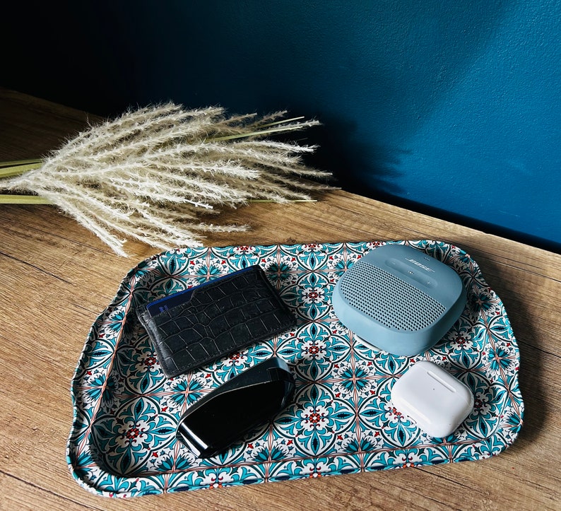 May include: A blue and white patterned tray with a black leather wallet, a blue speaker, and a white wireless earbud.