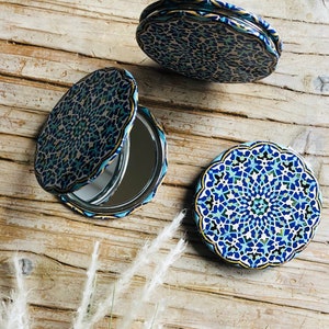 May include: Three round, compact mirrors with blue and gold patterned designs. The mirrors are closed and feature intricate geometric patterns.