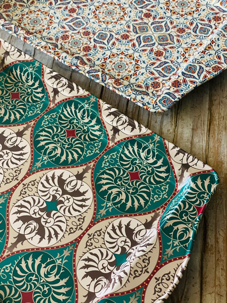 May include: Two decorative trays with intricate patterns. The top tray has a white background with blue, red, and brown floral designs. The bottom tray has a teal background with brown and white floral designs.