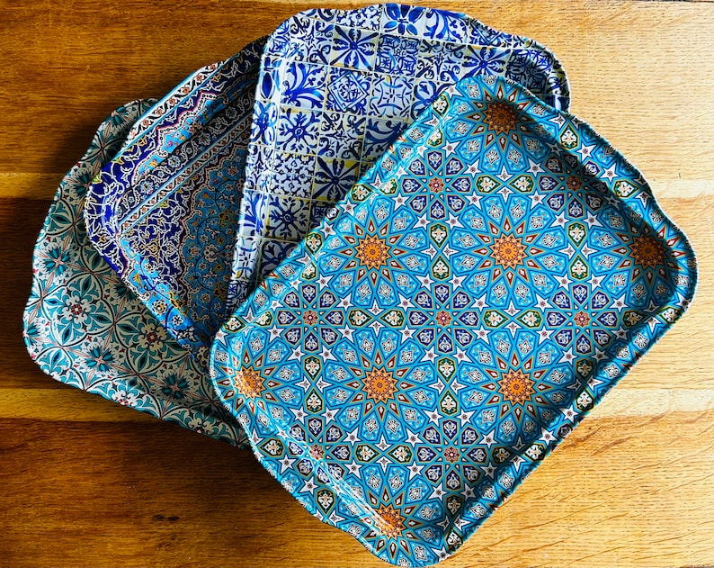 May include: Four blue and white ceramic trays with intricate geometric patterns. The trays are stacked on top of each other, with the largest tray on the bottom and the smallest tray on top.