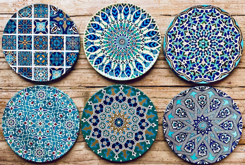 May include: Six decorative ceramic plates with intricate blue, green, and gold geometric patterns. The plates have a white background and are arranged in a row on a wooden surface.