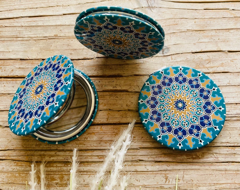May include: Three round, compact mirrors with a blue, gold, and white geometric pattern. The mirrors are closed and feature a traditional design.