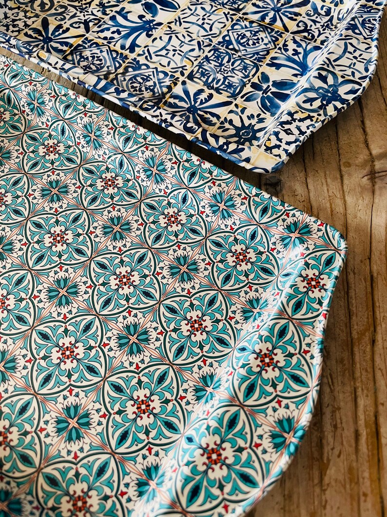 May include: Two decorative trays with a blue and white tile pattern. The top tray has a more intricate design with a yellow background. The bottom tray has a simpler design with a white background.