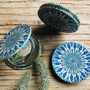 May include: Three round compact mirrors with a blue and white mandala design. The mirrors are closed and feature a silver reflective surface.