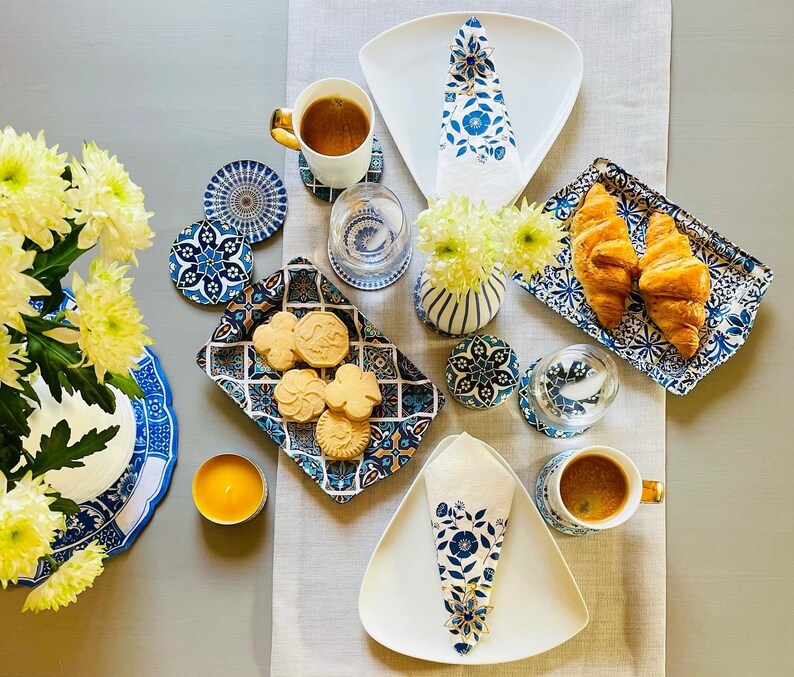 May include: A table setting with blue and white patterned plates, coasters, and napkins. There are also croissants, cookies, and a candle on the table.