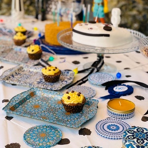 May include: A table setting with blue and white patterned coasters, a blue and white patterned tray, and a yellow candle in a blue and white patterned container. There are also cupcakes with yellow frosting and chocolate sprinkles on the tray.
