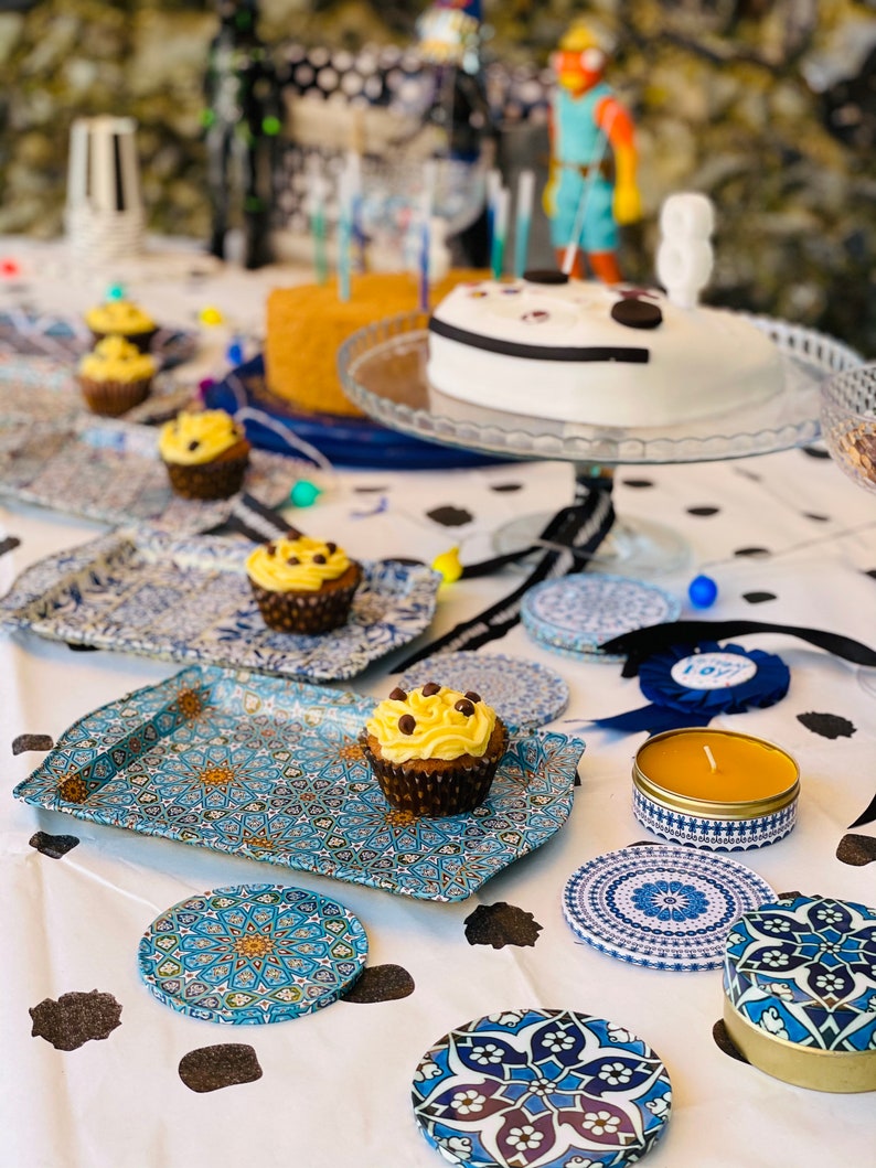 May include: A table setting with blue and white patterned coasters, a blue and white patterned tray, and a yellow candle in a blue and white patterned container. There are also cupcakes with yellow frosting and chocolate sprinkles on the tray.