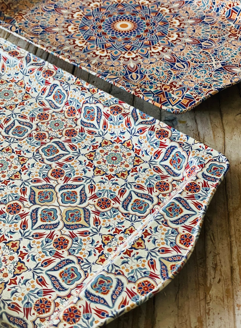 May include: Two rectangular serving trays with a white background and intricate blue, red, and gold floral patterns. The trays are made of metal and have a slightly raised edge.