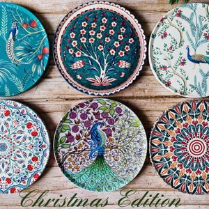 May include: Six decorative ceramic plates with various colourful patterns featuring peacocks, flowers, and geometric designs. The plates are arranged in a circular pattern on a wooden surface. The text "Christmas Edition" is written below the plates.
