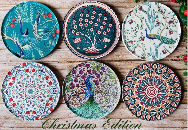 May include: Six decorative ceramic plates with various colourful patterns featuring peacocks, flowers, and geometric designs. The plates are arranged in a circular pattern on a wooden surface. The text "Christmas Edition" is written below the plates.
