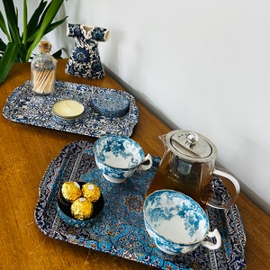 May include: Two blue and white patterned trays with a teapot, teacups, and chocolates. One tray has a candle and matches in a glass bottle.