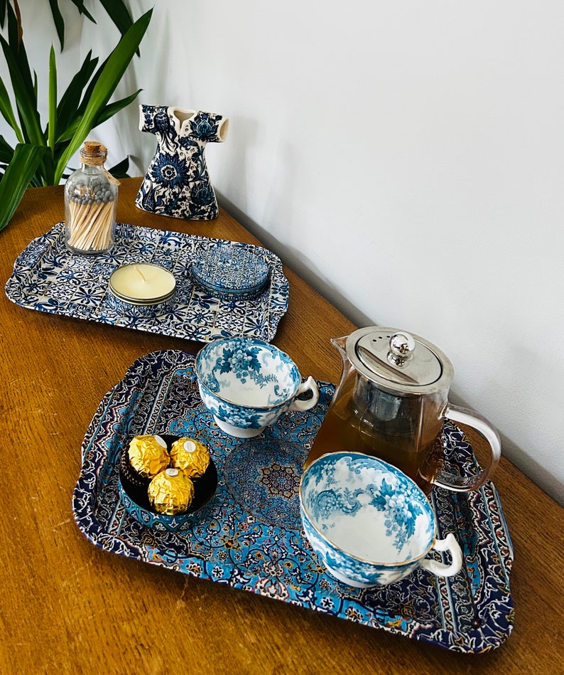 May include: Two blue and white patterned trays with a teapot, teacups, and chocolates. One tray has a candle and matches in a glass bottle.