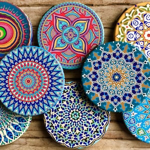 May include: Seven colorful round coasters with intricate geometric patterns in shades of blue, green, red, yellow, and white. The coasters are made of ceramic and have a glossy finish.