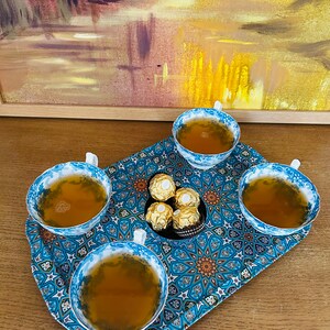 May include: A blue and gold patterned tray with four teacups filled with tea and a small dish of chocolate candies in the center.