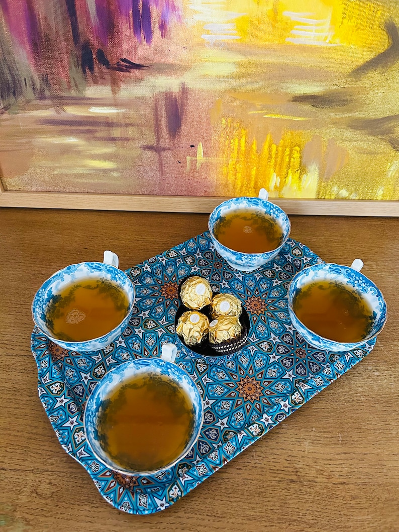 May include: A blue and gold patterned tray with four teacups filled with tea and a small dish of chocolate candies in the center.