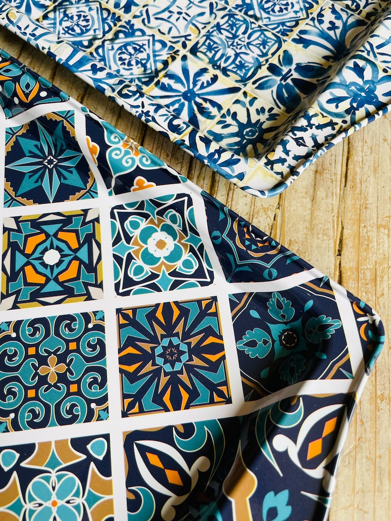 May include: Two metal serving trays with a blue and white geometric tile pattern. The trays are made of metal and have a white background with blue and white geometric designs.