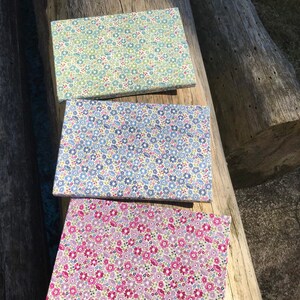 Könnte beinhalten: Drei Stoffquadrate mit einem Blumenmuster. Das obere Quadrat ist grün mit weißen Blumen, das mittlere Quadrat ist blau mit weißen Blumen und das untere Quadrat ist rosa mit weißen Blumen.