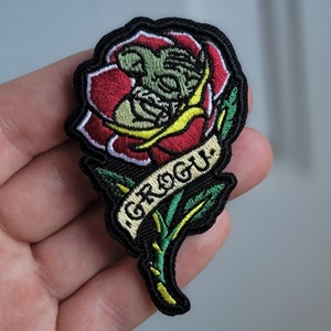 Op de afbeelding: Een geborduurde strijk-patch met een groen Grogu-personage in een rode roos met een banner waarop "Grogu" staat.