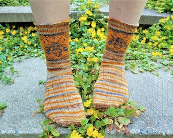 Peut inclure: Une paire de chaussettes tricotées à la main avec un motif rayé dans des tons d'orange, de brun et de blanc. Les chaussettes présentent un motif d'abeille sur le dessus du pied.