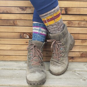 May include: A pair of brown leather hiking boots with brown laces. The boots are worn and have a distressed look. The person wearing the boots is also wearing a pair of colorful knitted socks.