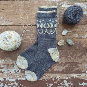 Puede incluir: Un par de calcetines de punto grises con un patrón geométrico blanco y amarillo. Los calcetines están sobre una superficie de madera.