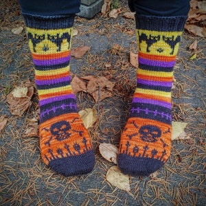 May include: A pair of black, orange, yellow, and purple striped socks with a black cat and skull design. The socks are knitted and have a Halloween theme.