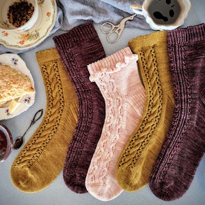 May include: Four pairs of knitted socks in different colours, including mustard yellow, pink, and burgundy. The socks are all patterned with a cable knit design.
