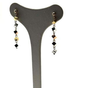 Op de afbeelding: Een paar gouden, zilveren en ros&eacute;gouden oorhangers met een ketting van kleine kubusvormige kralen.