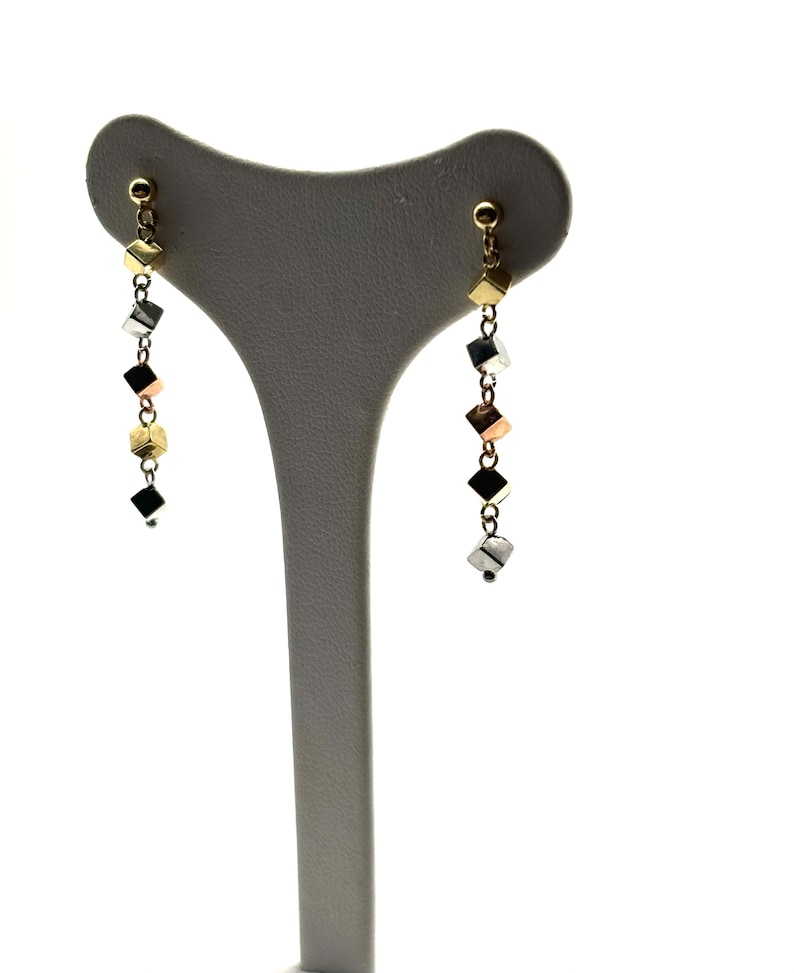 Op de afbeelding: Een paar gouden, zilveren en ros&eacute;gouden oorhangers met een ketting van kleine kubusvormige kralen.