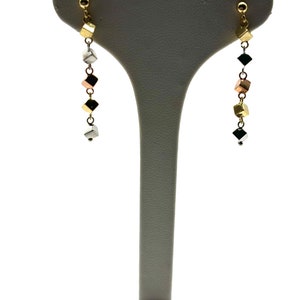 Op de afbeelding: Een paar gouden, zilveren en ros&eacute;gouden oorhangers met een ketting van kleine vierkante kralen.