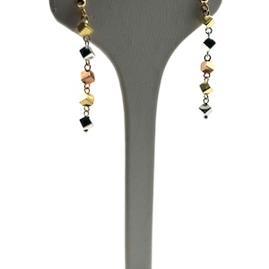 Op de afbeelding: Een paar gouden, zilveren en ros&eacute;gouden oorhangers met een ketting van kleine vierkante kralen.