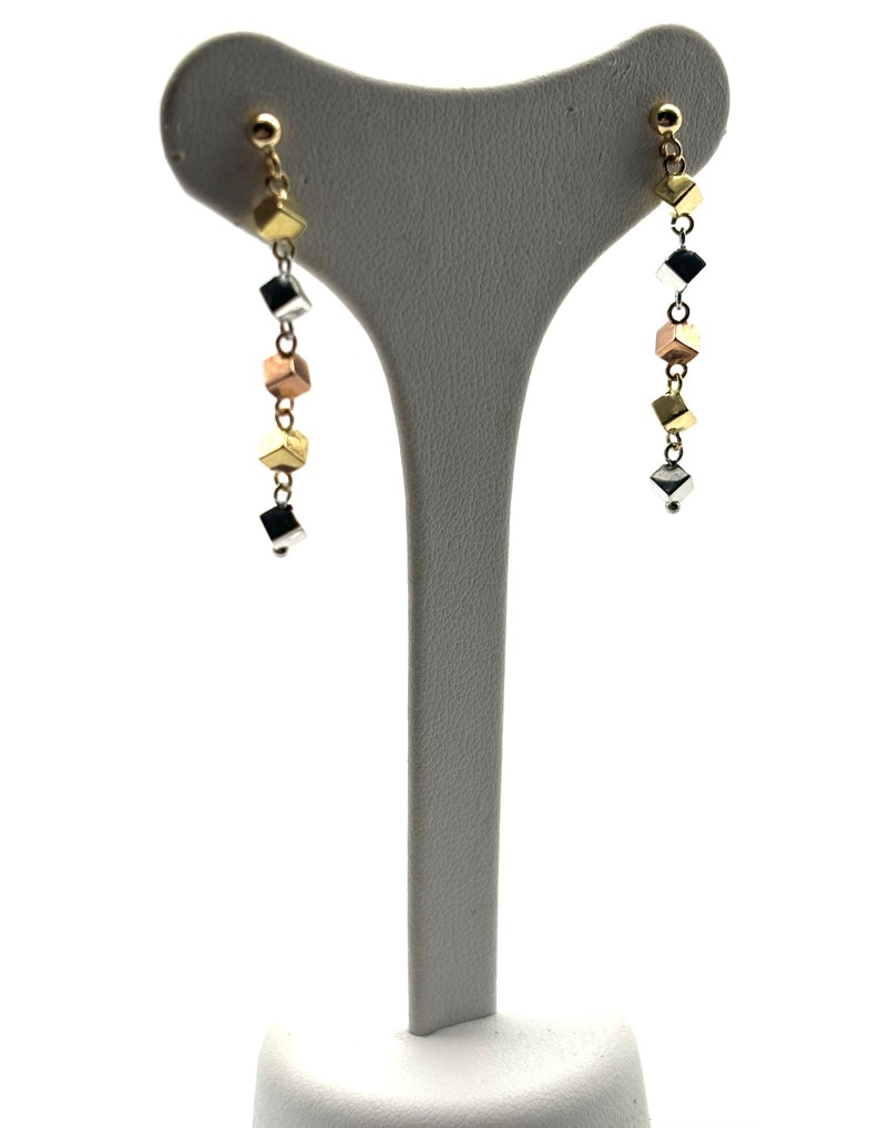 Op de afbeelding: Een paar gouden, zilveren en ros&eacute;gouden oorhangers met een ketting van kleine vierkante kralen.