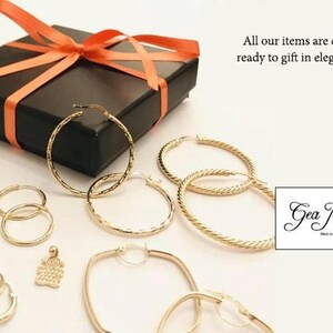May include: A set of gold hoop earrings in various sizes and styles, including a pair of square hoops, a pair of textured hoops, and a pair of plain hoops. The earrings are displayed on a white surface with a black gift box and a small tag that reads "Gea Jewelry Made in Italy".