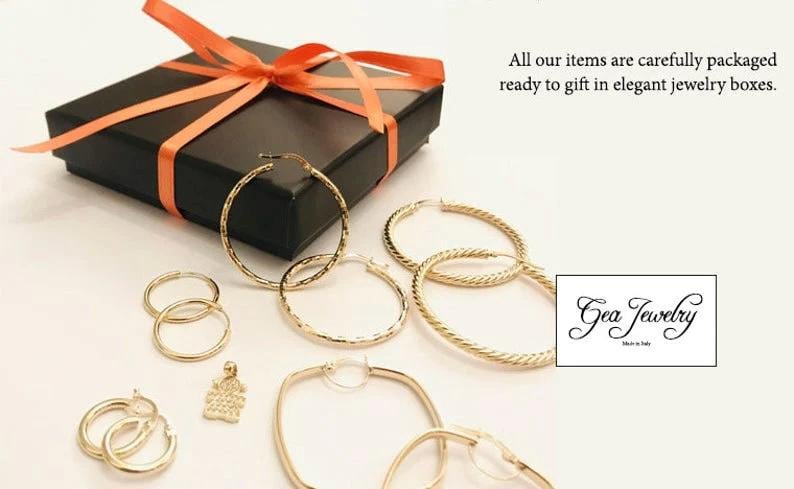 May include: A set of gold hoop earrings in various sizes and styles, including a pair of square hoops, a pair of textured hoops, and a pair of plain hoops. The earrings are displayed on a white surface with a black gift box and a small tag that reads "Gea Jewelry Made in Italy".