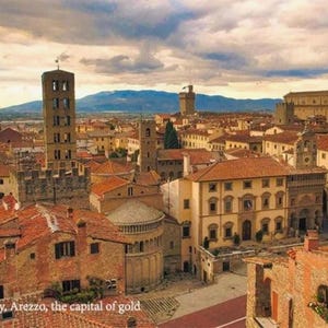 Pode incluir: Uma vista a&eacute;rea de uma cidade italiana hist&oacute;rica com edif&iacute;cios de cor terracota, uma torre alta e uma grande muralha de pedra. A cidade &eacute; cercada por colinas onduladas e um c&eacute;u nublado.