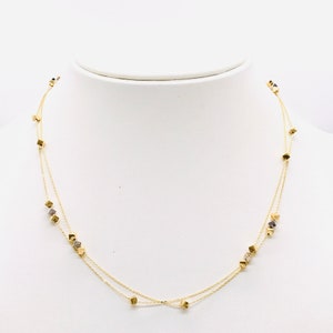 Op de afbeelding: Een gouden ketting met twee kettingstrengen en kleine vierkante bedels.