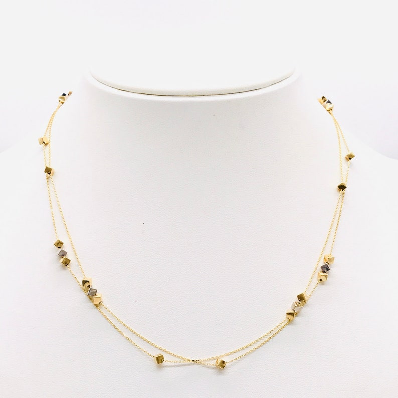 Op de afbeelding: Een gouden ketting met twee kettingstrengen en kleine vierkante bedels.